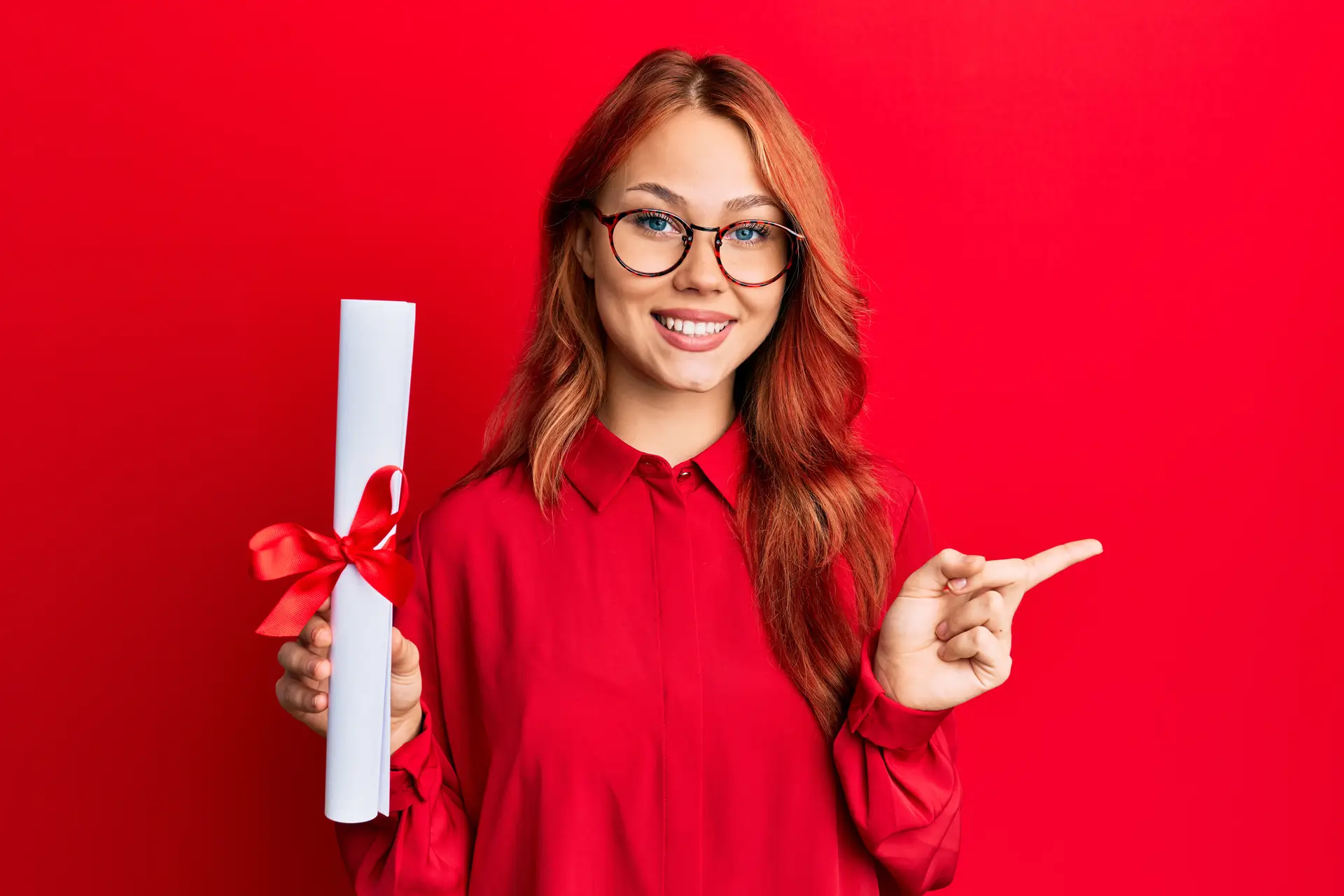 Young redhead woman holding graduate degree diploma smiling happy pointing with hand and finger to the side